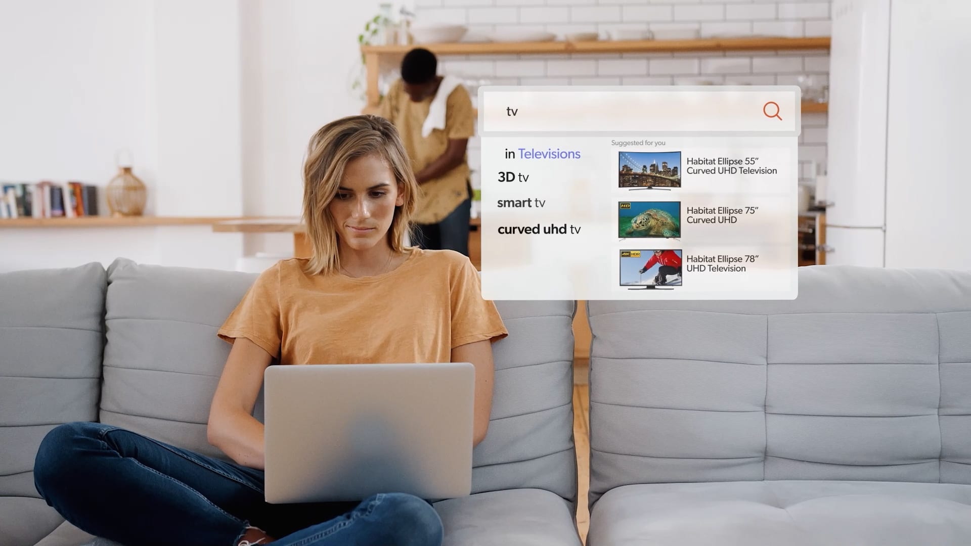 A woman sitting on a couch gets suggestions for TVs from a search bar.