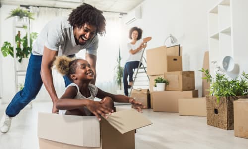 African American father pushing daughter in box while moving into a house