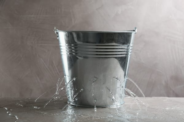 Leaky bucket with water on table against grey background