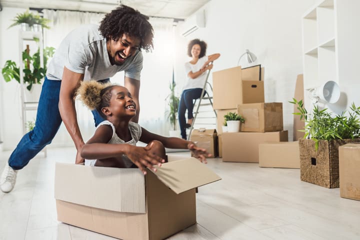 African American father pushing daughter in box while moving into a house
